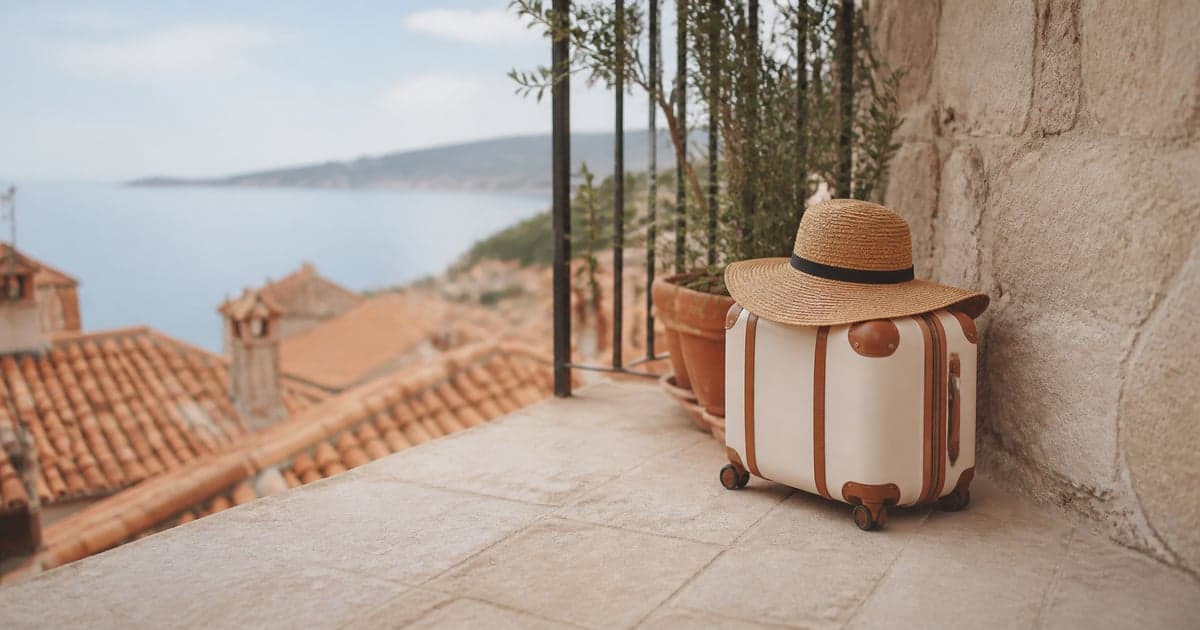 a small suitcase and a straw sunhat on a tiled hotel balcony above terracotta rooftops
