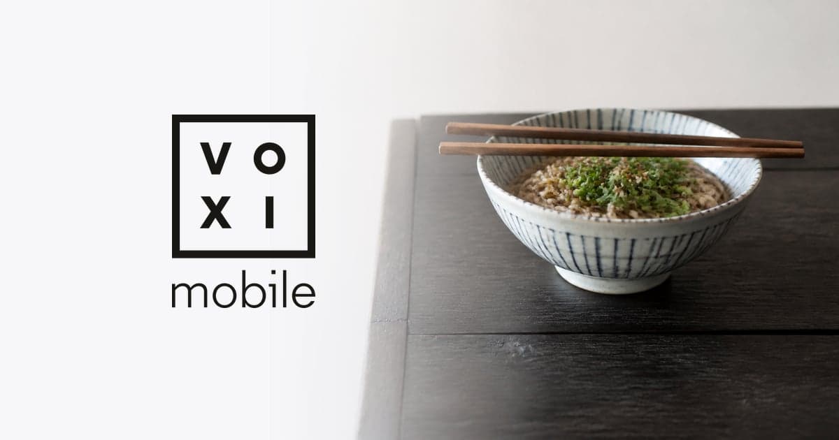 a bowl of noodles with chopsticks resting across it on a dark wooden table